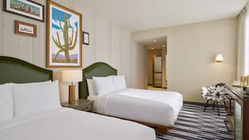 A hotel room with two beds, a desk, a chair, and a wall with framed pictures.