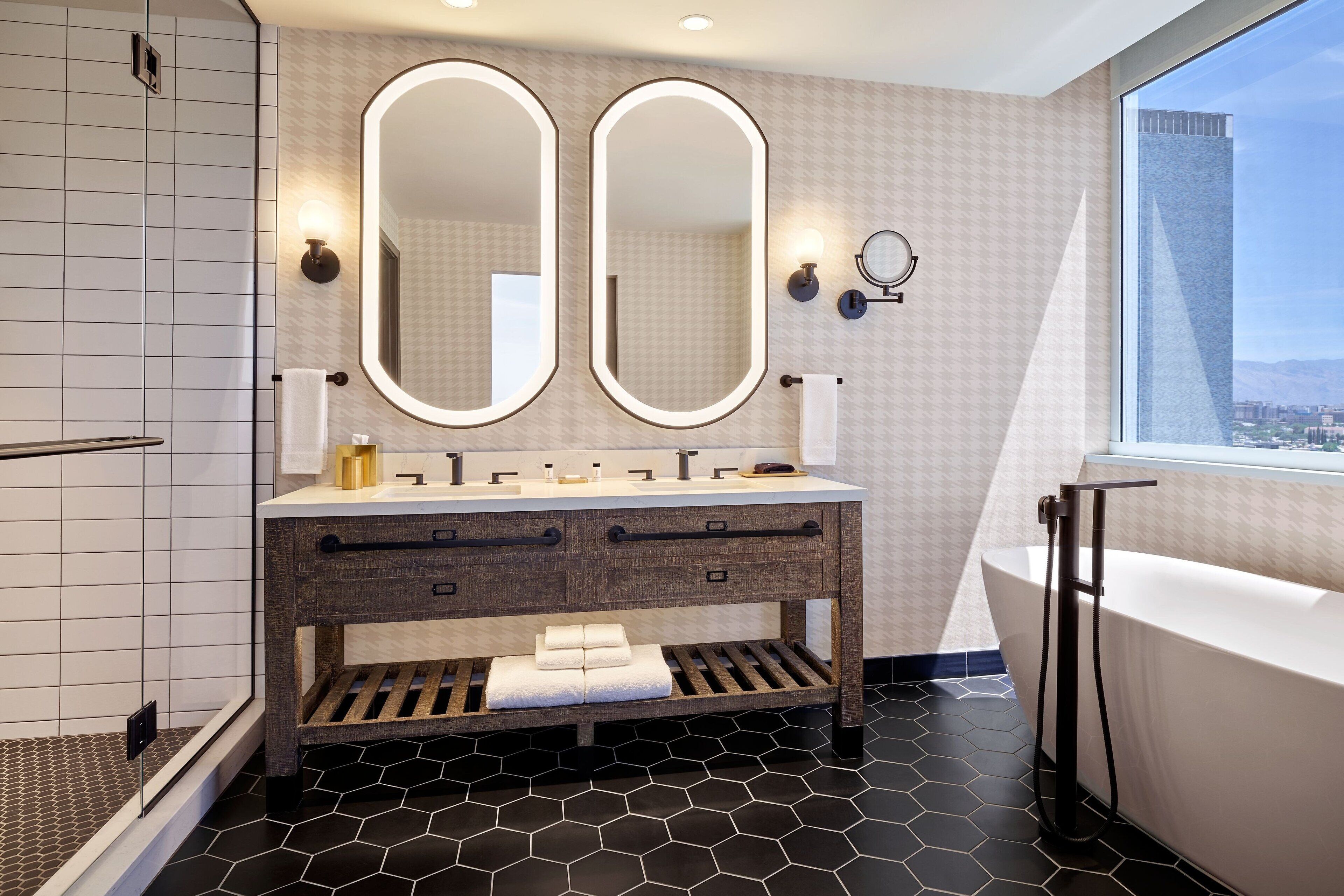 A modern bathroom with a large vanity, two mirrors, a bathtub, and a city view.