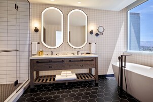 Un baño moderno con un tocador amplio, dos espejos, una bañera y vista a la ciudad.