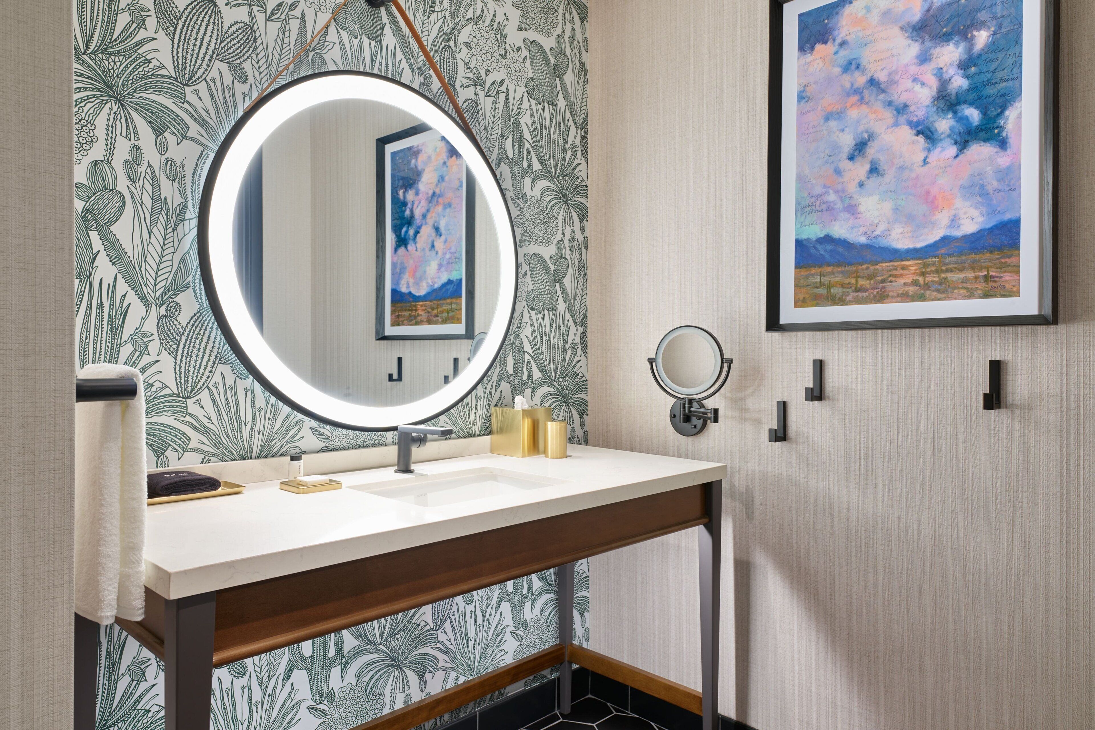 Un bagno con uno specchio rotondo, un lavandino e un porta asciugamani. Al muro, un quadro incorniciato e uno specchio tondo sopra il lavandino.