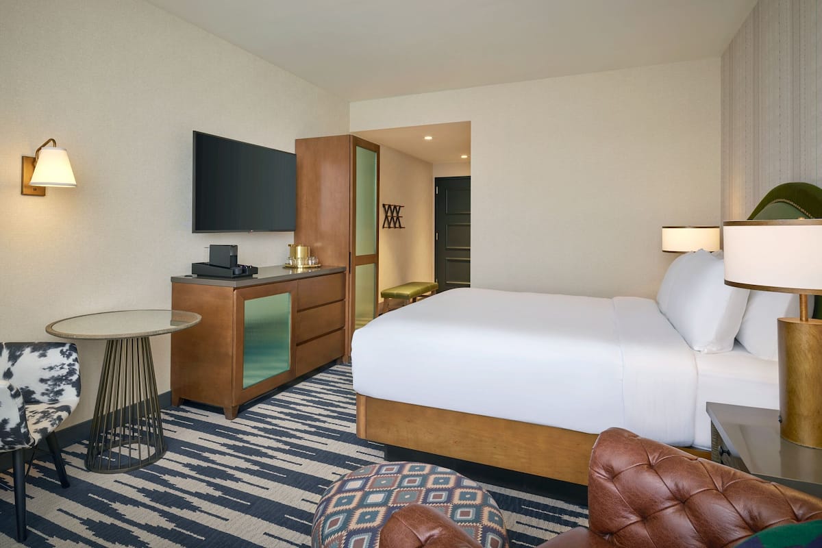 A hotel room with a large bed, a desk with a computer, a chair, a small table, and a TV on the wall.