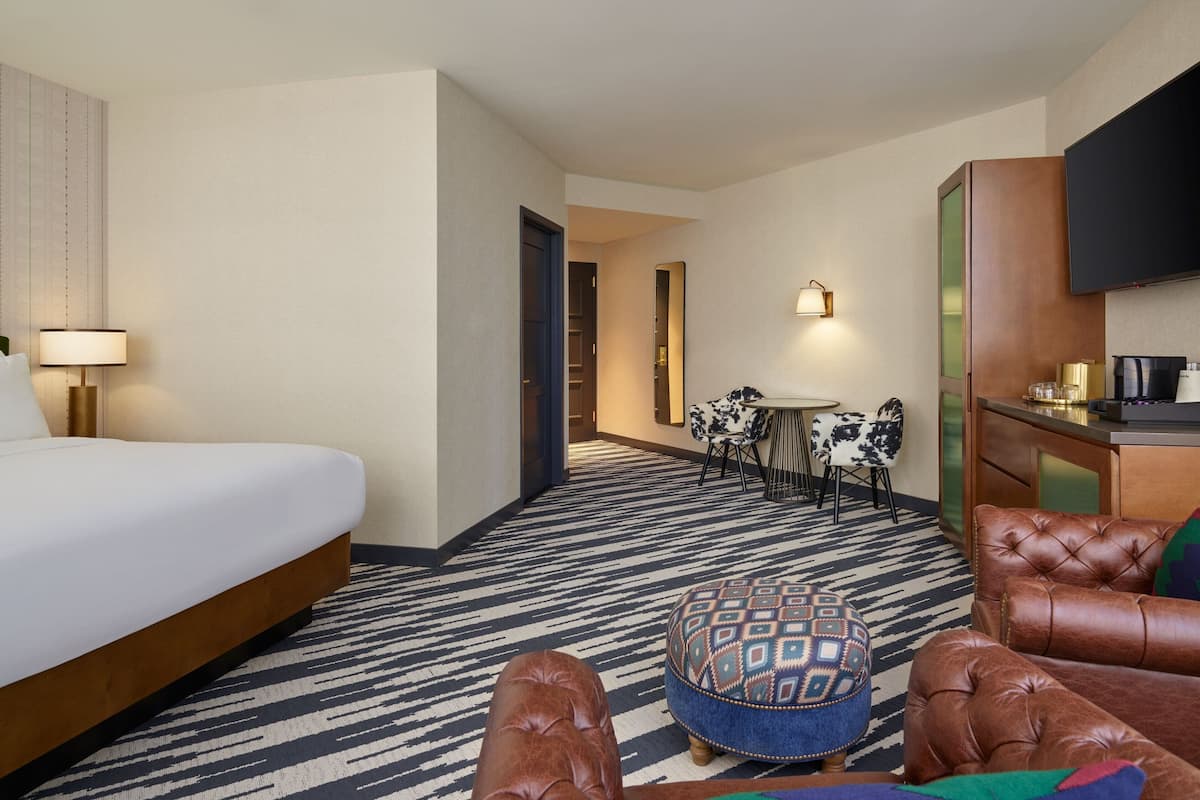 A hotel room with a bed, a desk, a chair, and a sofa.