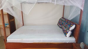 Un letto singolo con un materasso bianco e un cuscino colorato, coperto da una zanzariera.