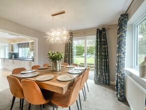 A dining area with a wooden table set for six, surrounded by orange chairs, a potted plant, and a modern chandelier. - Broadsands (Paignton)