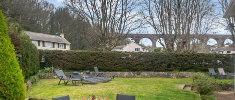 An outdoor dining area with a table and chairs, a fire pit, and a view of a bridge in the background.