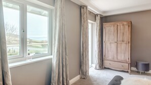 A bedroom with a large window, a wardrobe, and a bench. - Broadsands (Paignton)