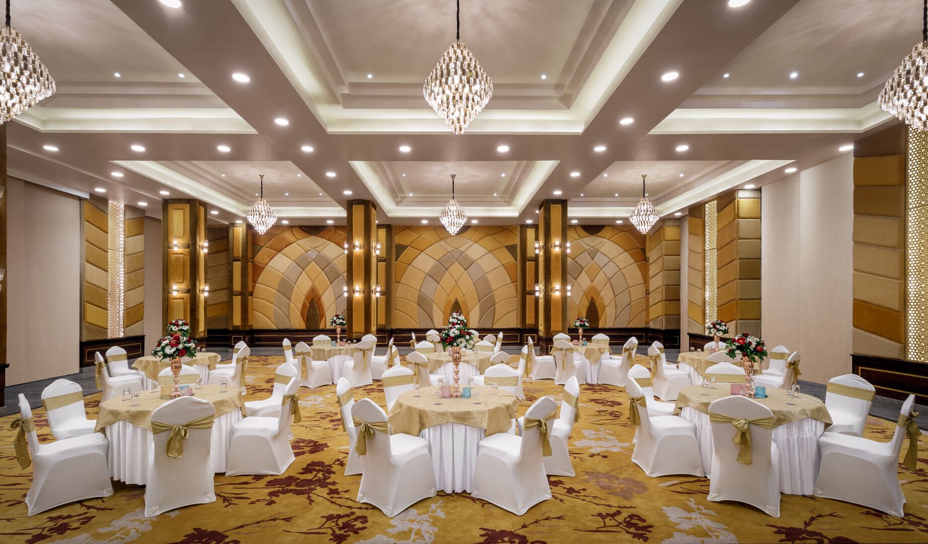 Un salón de banquetes con mesas redondas, sillas blancas y cintas doradas.