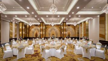 Un salón de banquetes con mesas redondas, sillas blancas y cintas doradas.