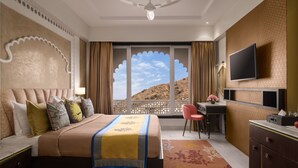 A hotel room with a bed, desk, chair, and a TV on the wall. - juSTa Ssatva Resort - Udaipur (Udaipur)