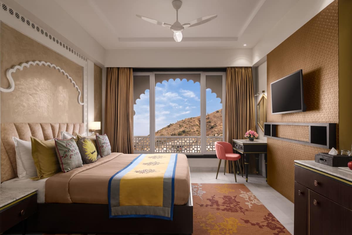 A hotel room with a bed, desk, chair, and a TV on the wall.