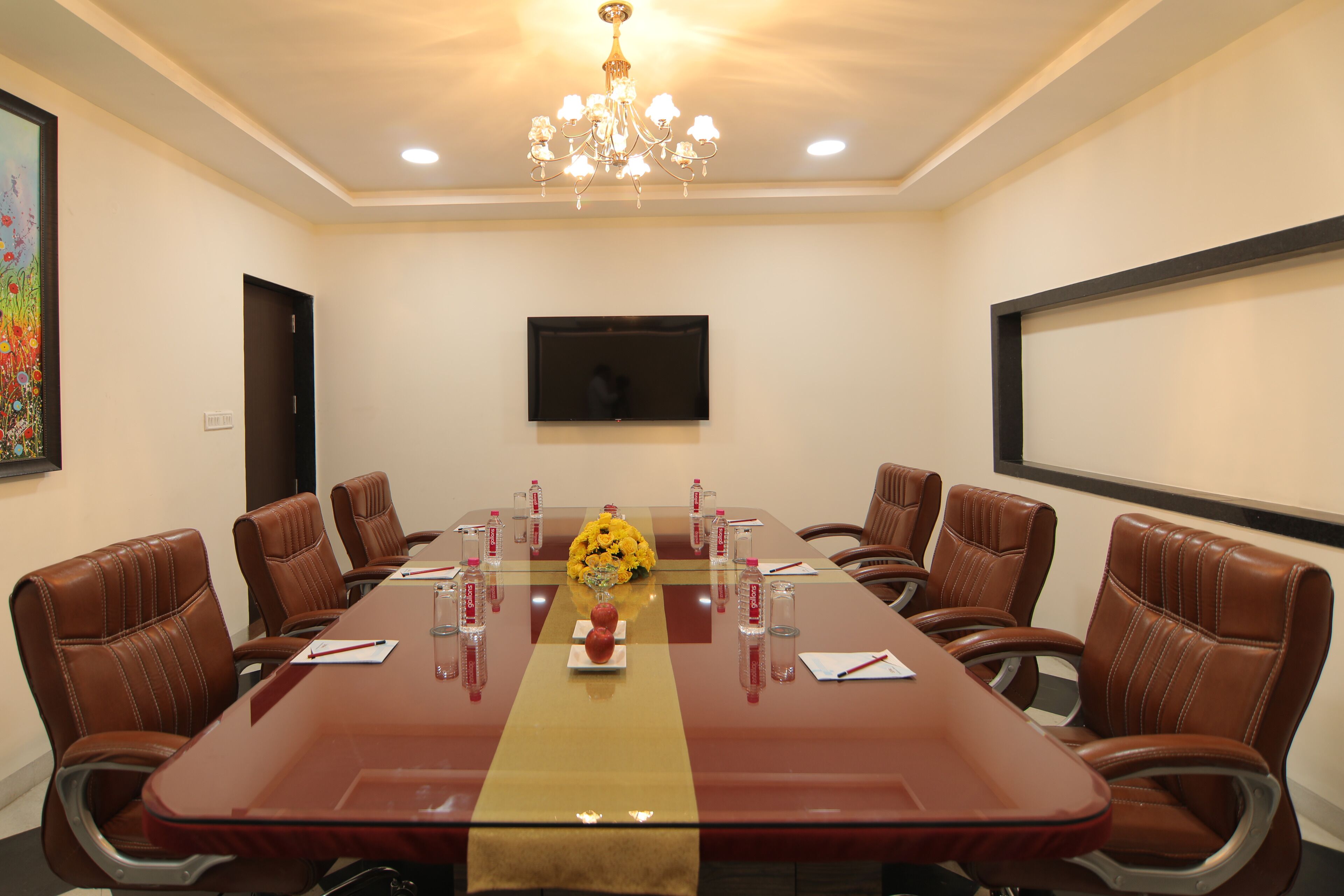 A conference room with a long table, leather chairs, a chandelier, a TV, and a floral centerpiece.