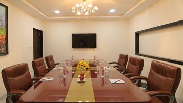 A conference room with a long table, leather chairs, a chandelier, a TV, and a floral centerpiece.