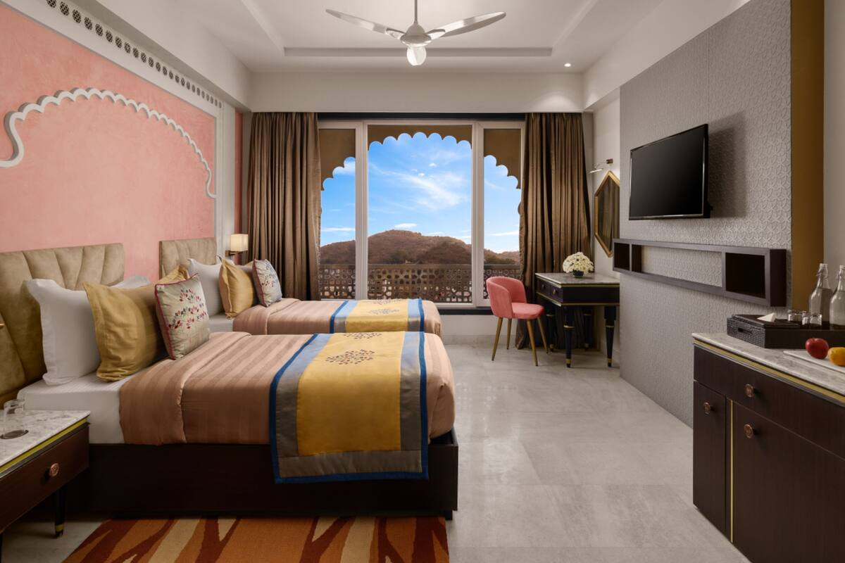 A hotel room with a large bed, a desk, a television, and a view of the mountains.