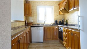 A kitchen with wooden cabinets, a white dishwasher, and a window above the sink. - Cosy villa with private pool and sea and mountain views, in Denia (Denia)