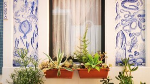 A window with blue marine life tiles, a curtain, and two hanging flower pots with plants. - Frutas do Mar apartamento (Portimão)