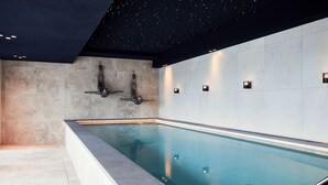 Ein modernes Hallenbad mit glasklarer Wasseroberfläche, dunkler Decke mit sternförmigen Lichtern und schlichter Wandgestaltung.