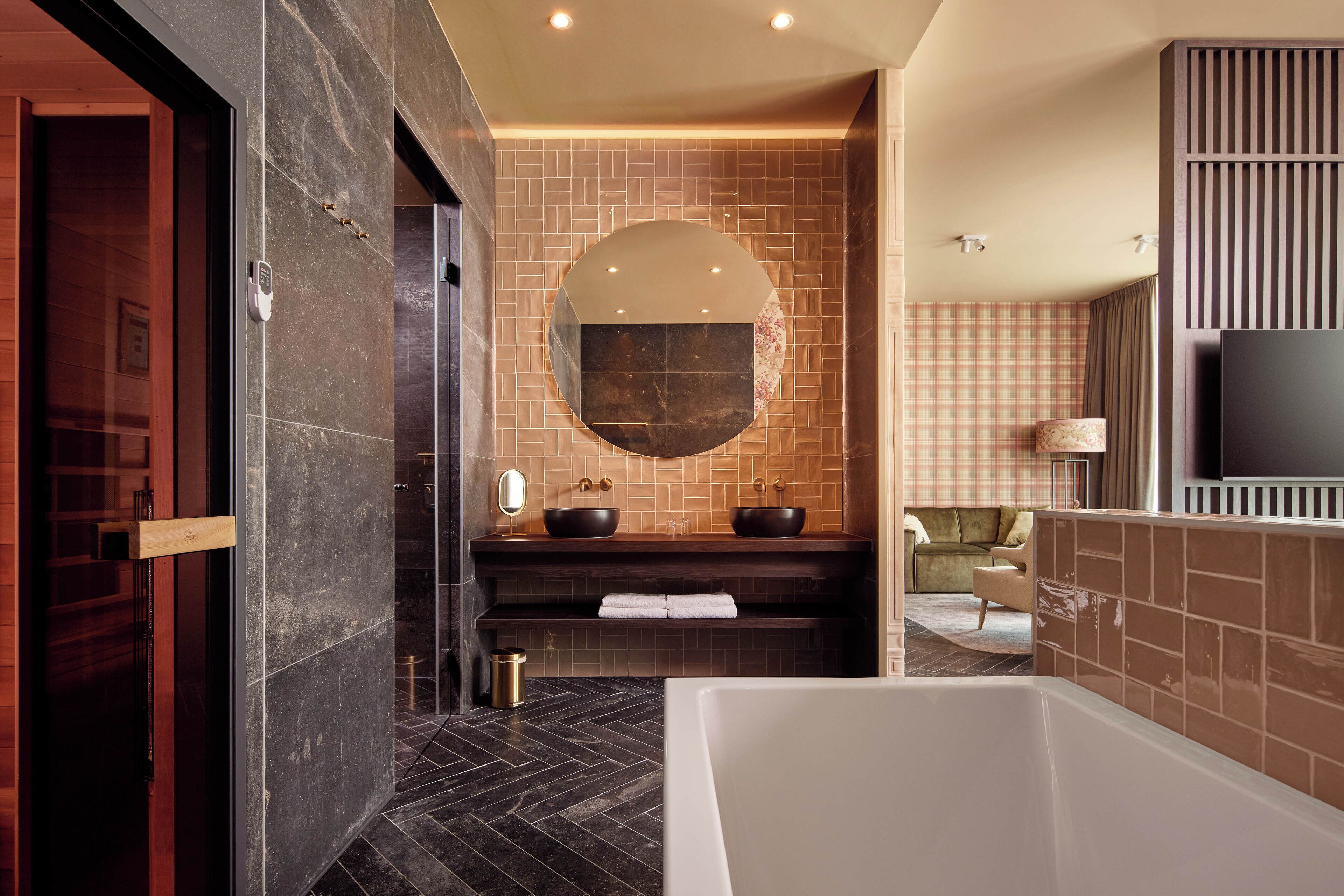 Un baño moderno con una bañera grande, un espejo redondo y dos lavamanos negros.