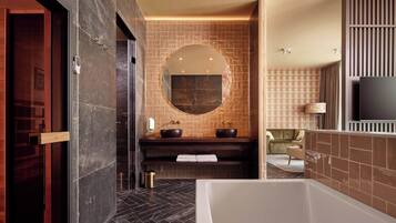 Un baño moderno con una bañera grande, un espejo redondo y dos lavamanos negros.