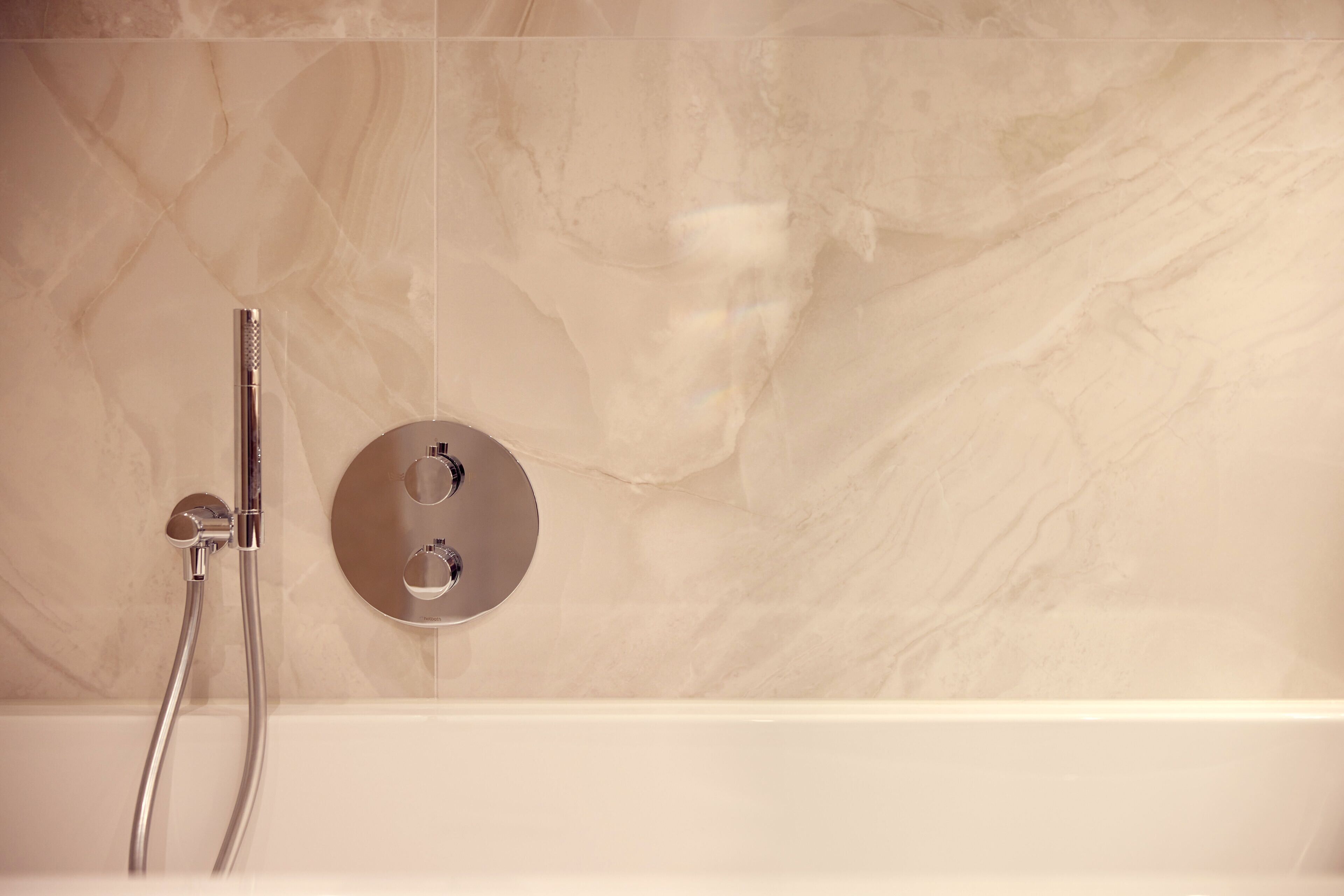 A modern bathroom with a marble wall, a bathtub, and a shower with two chrome fixtures.