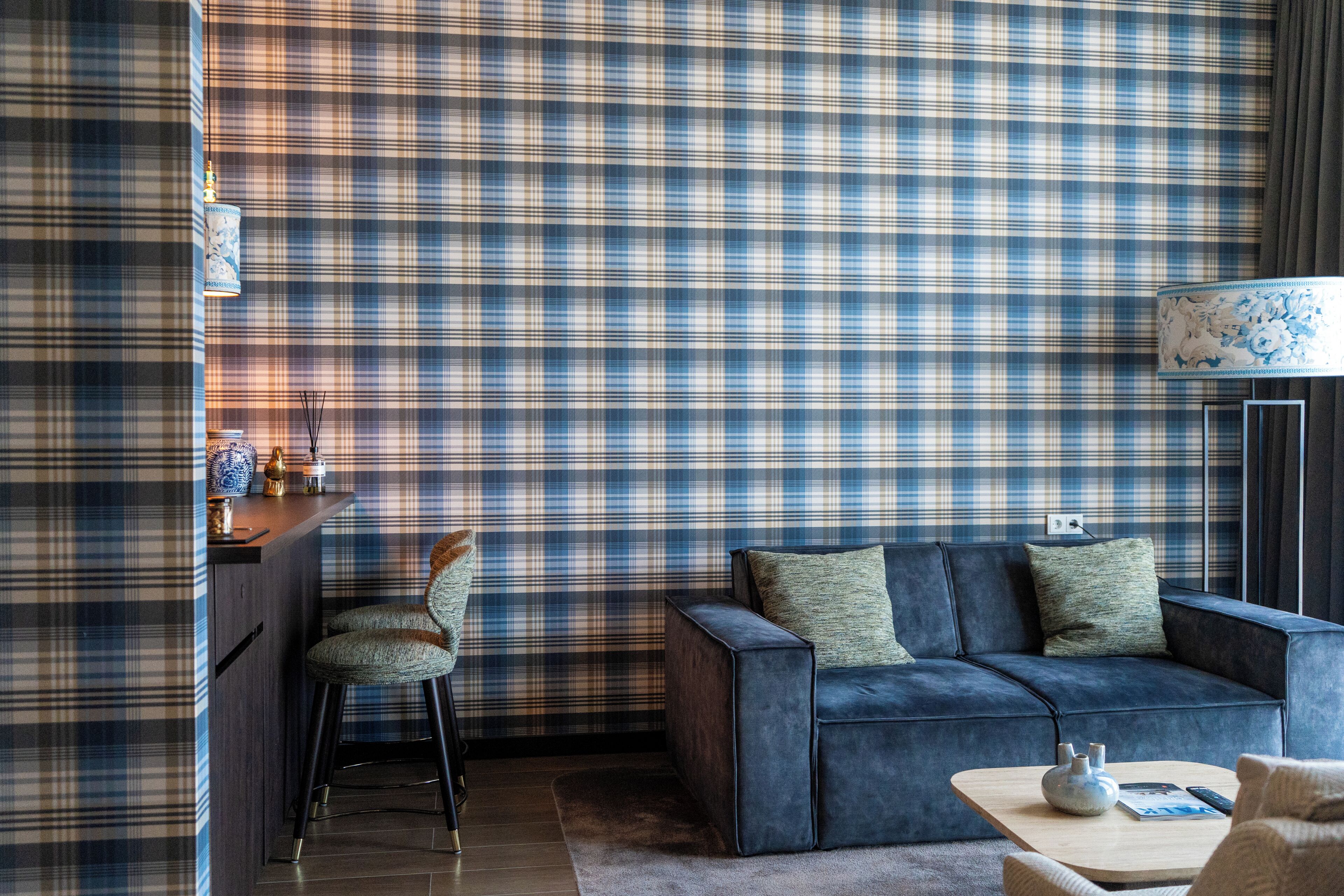 A modern living room with a blue sofa, a small coffee table, and a plaid-patterned wall.