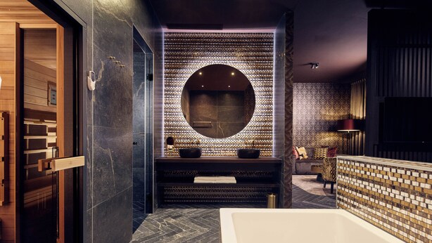 Ein modernes Badezimmer mit einer großen Badewanne, einem runden Spiegel und einer gefliesten Wand.