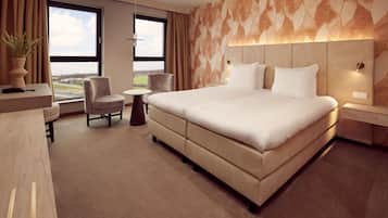 A modern hotel room with a large bed, a desk, a chair, and a small table.