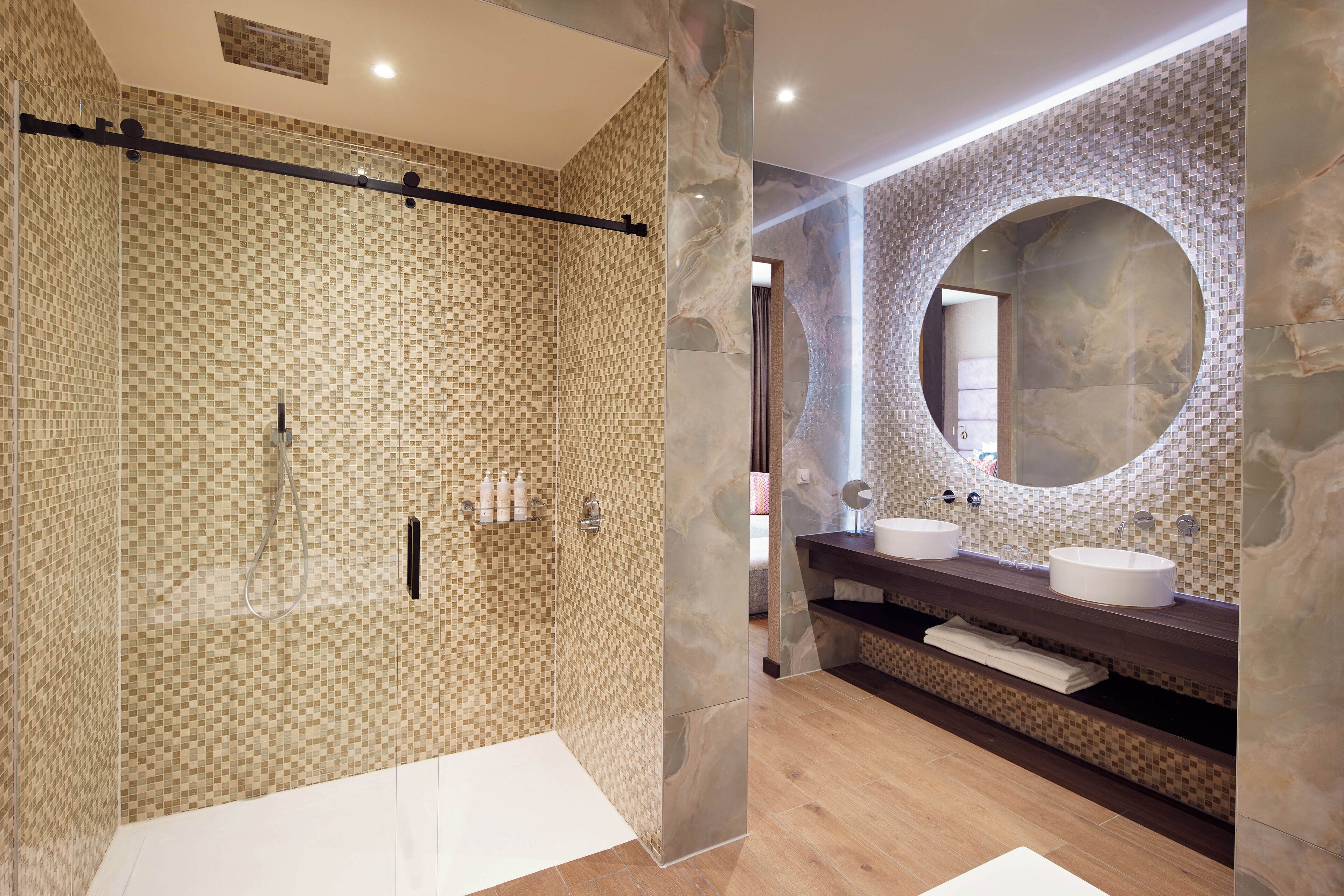 Un baño moderno con ducha envuelta en vidrio, pared de azulejos de mármol y un espejo grande sobre el lavabo.