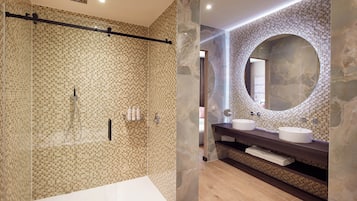 Un baño moderno con ducha envuelta en vidrio, pared de azulejos de mármol y un espejo grande sobre el lavabo.