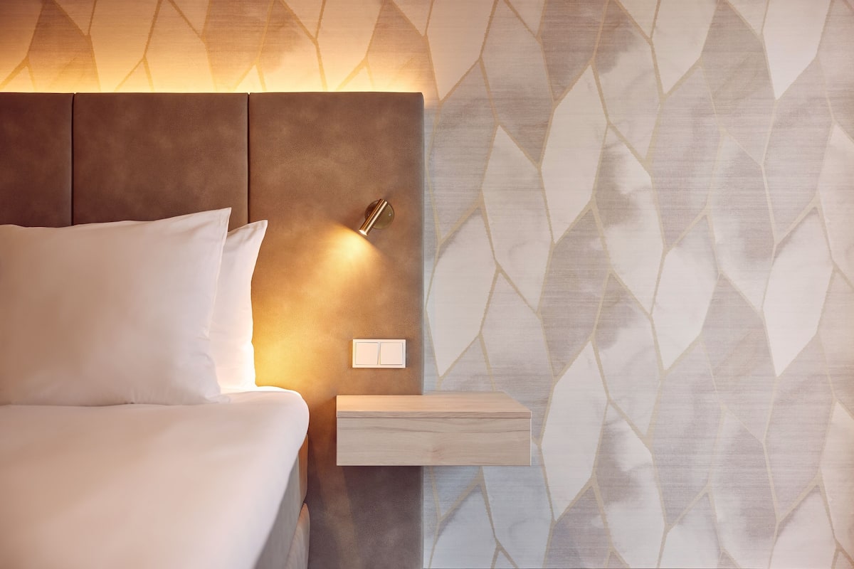 Ein modernes Hotelzimmer mit einem Bett, einem Nachttisch und einer Wand mit geometrischem Muster.