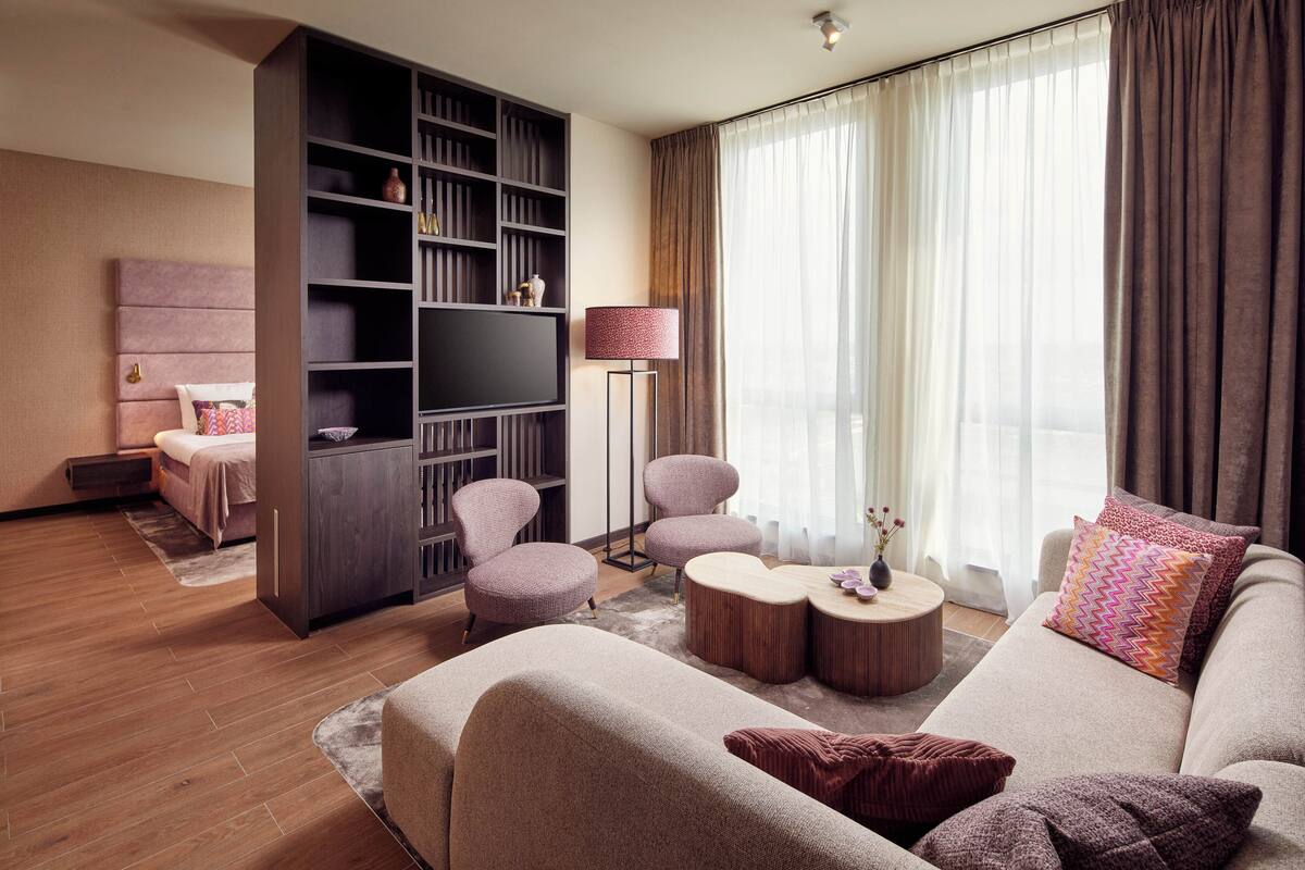 Ein modernes Wohnzimmer mit einer Couch, zwei Sesseln, einem Couchtisch, einem Bücherregal und einem Flachbildfernseher.