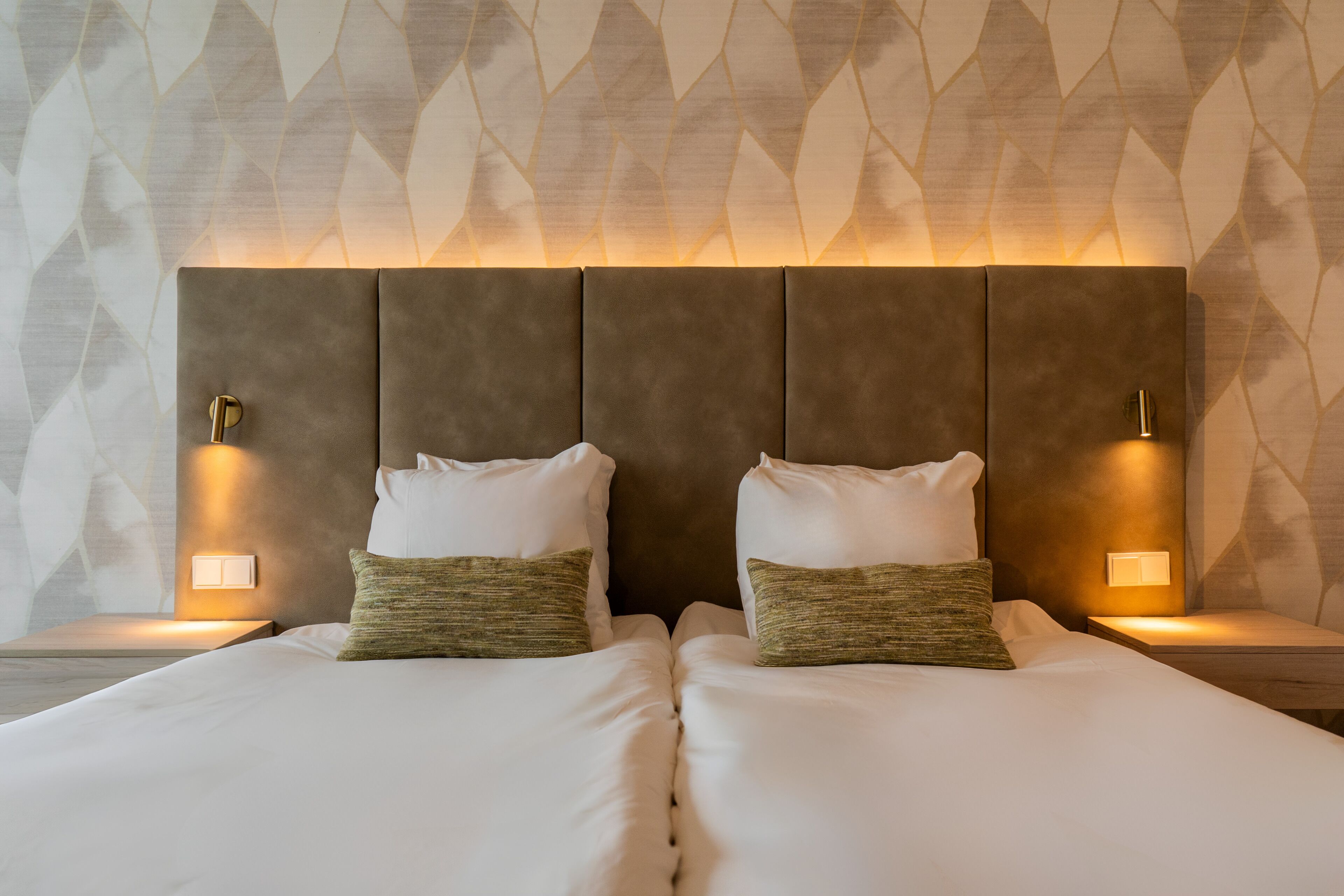 A double bed with two pillows, a headboard with integrated lighting, and a patterned wall in the background.