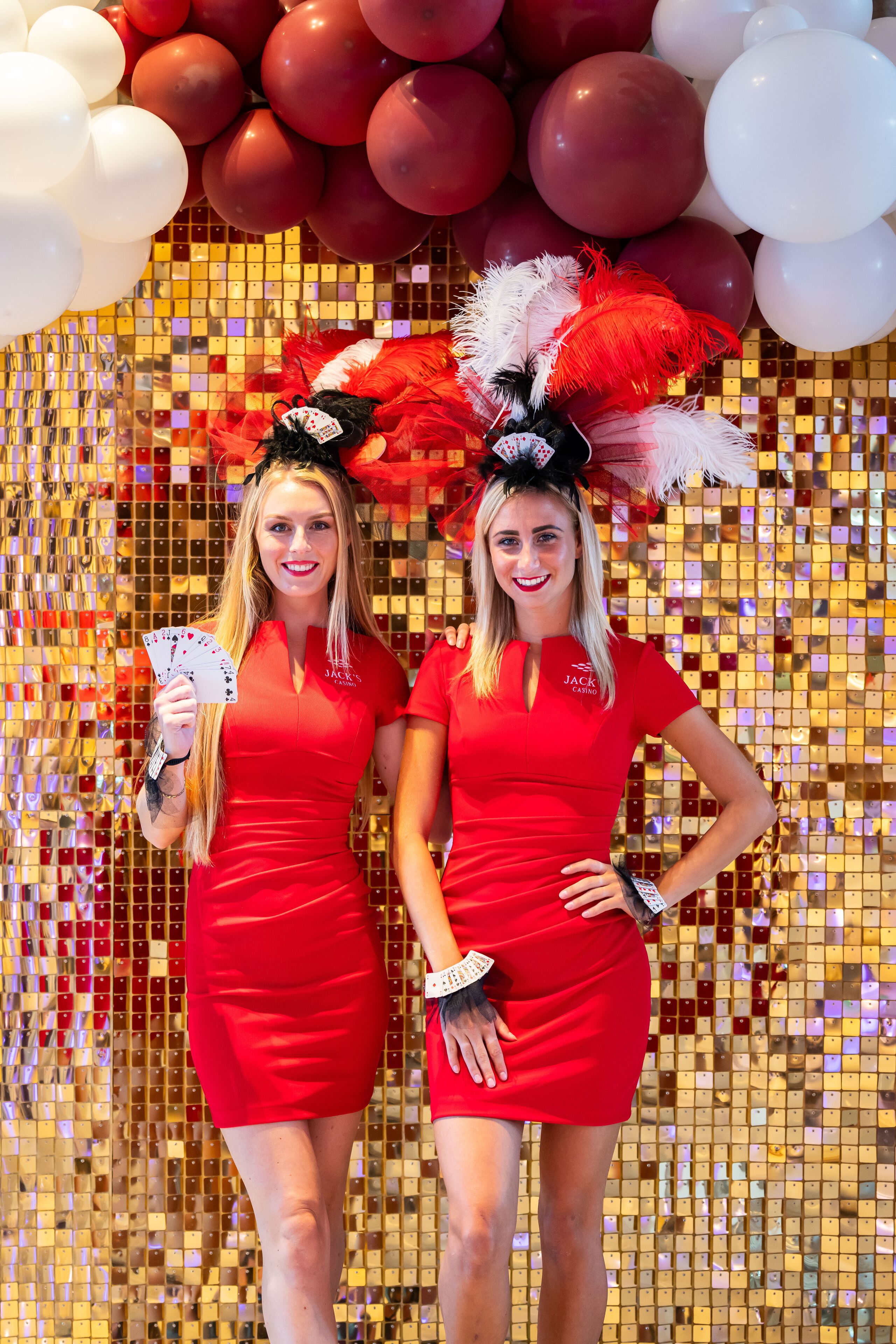 Dos personas con vestidos rojos frente a una bola de discoteca y globos.