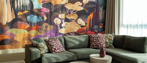 A living room with a green sofa, two white side tables, and a colorful abstract mural on the wall.