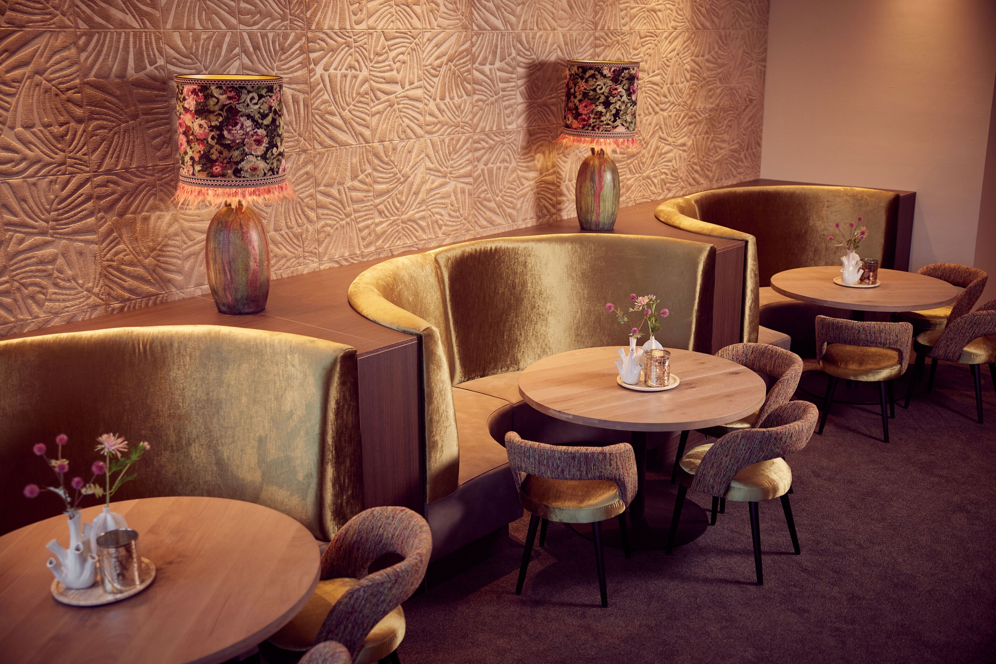 A modern lounge area with cushioned seating and round tables, each with a small vase of flowers.