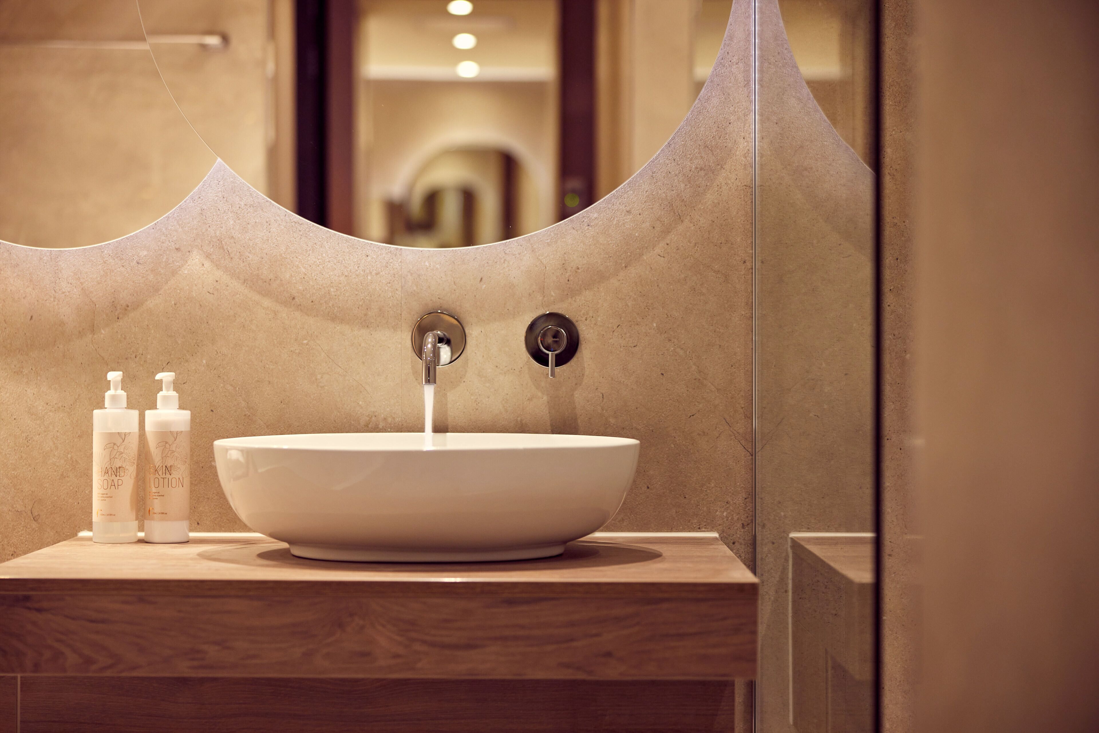 A bathroom with a large, round sink, two bottles of hand soap, and a mirror with a unique curved frame.