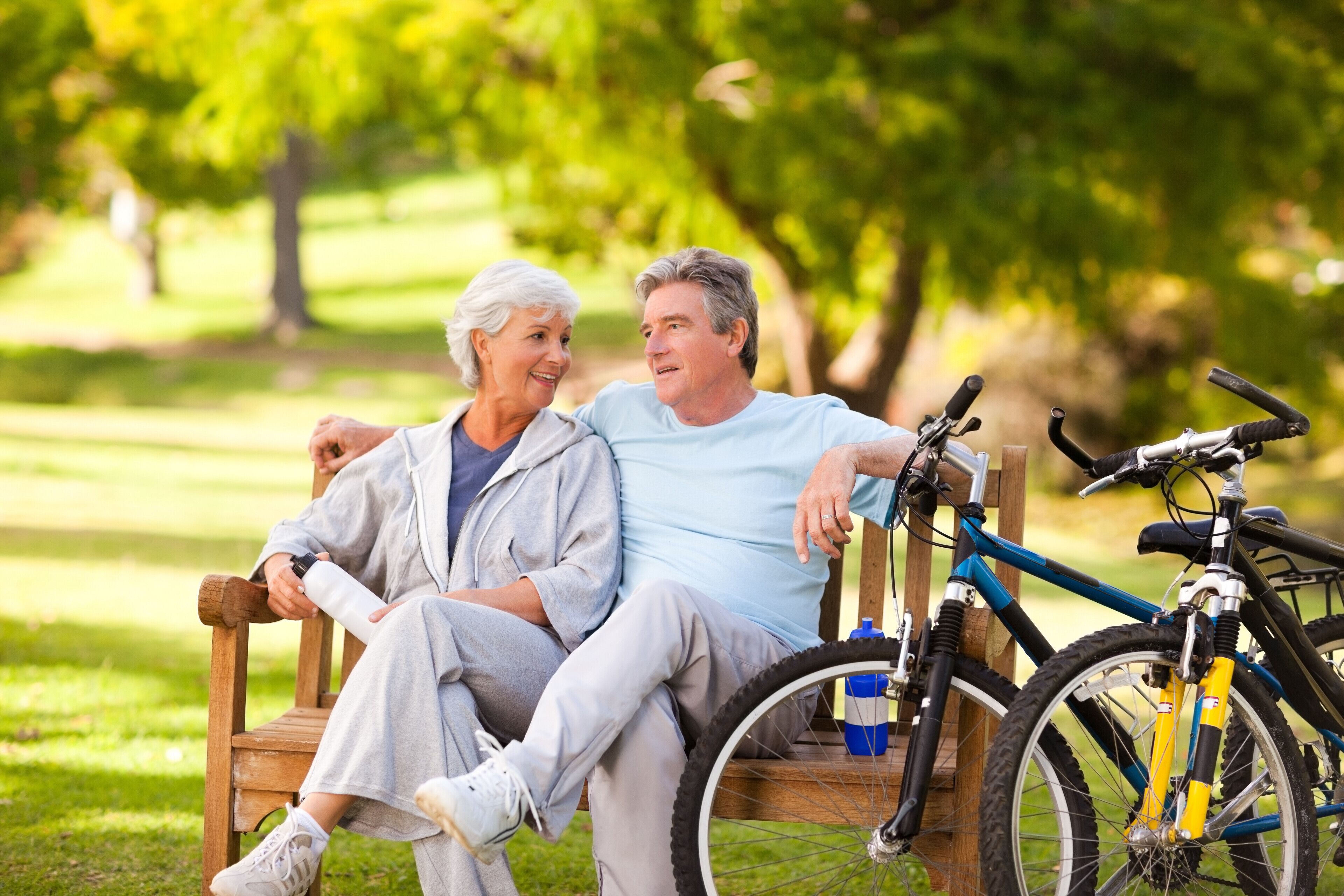 Un couple est assis sur un banc dans un parc, avec un vélo à côté d’eux.