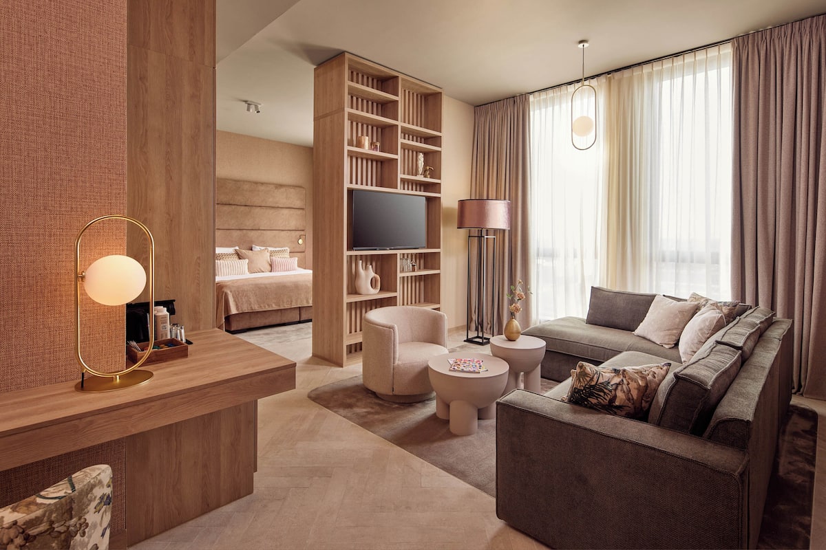 Ein modernes Hotelzimmer mit einem Holzbüro, einem großen Fernseher, einer Couch, einem runden Couchtisch und einem Nachttisch.
