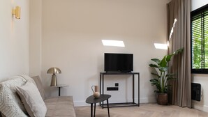Un salon moderne avec un canapé, une petite table sur laquelle se trouve une lampe, un téléviseur posé sur un meuble et une plante en pot.