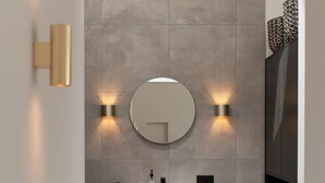 Une salle de bain moderne avec un grand miroir rond, deux appliques murales, un meuble-lavabo noir et un porte-serviettes.