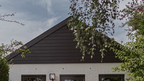 Une maison moderne avec une façade blanche, un toit foncé et un chemin en briques menant à une porte.