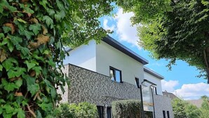 A modern two-story house with a white facade and stone accents, surrounded by lush greenery. - "achterwasser" - Moderne Ferienwohnung in Varel (Varel)