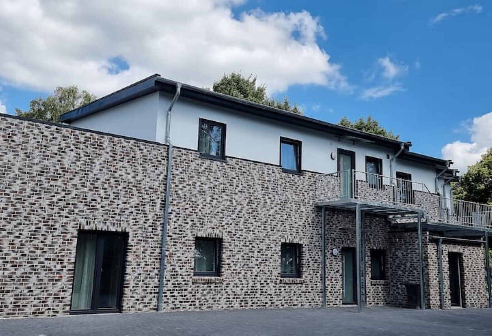 A modern building with a stone facade, multiple windows, and a flat roof.