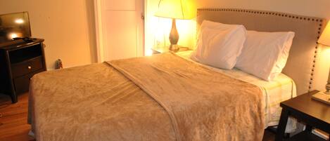 A bedroom with a bed, a nightstand, a lamp, and a television on a dresser.