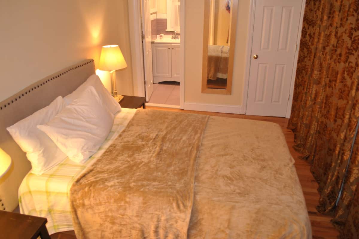 A bedroom with a bed, nightstand, lamp, and a door leading to a bathroom.