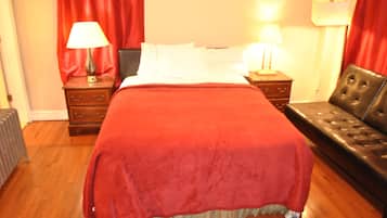 Quarto com uma cama grande, cortinas vermelhas, duas mesas de cabeceira com luminárias e uma poltrona de couro.