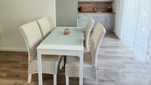 A dining area with a white table and wicker chairs, a kitchen in the background, and a hanging light fixture. - "steuerbord" - Moderne Ferienwohnung in Varel (Varel)