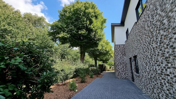 A narrow paved pathway flanked by lush greenery and a modern building with a brick facade. - "steuerbord" - Moderne Ferienwohnung in Varel (Varel)