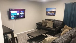 Una sala de estar con un sofá de cuero marrón oscuro, una mesa de centro y un televisor montado en la pared que muestra servicios de streaming.