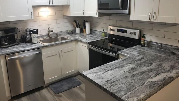 Una cocina moderna con gabinetes blancos, un lavavajillas de acero inoxidable, un microondas integrado y una estufa a gas.