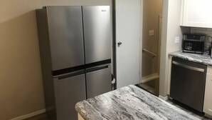 Cocina compacta con refrigerador de acero inoxidable, cafetera y lavavajillas.